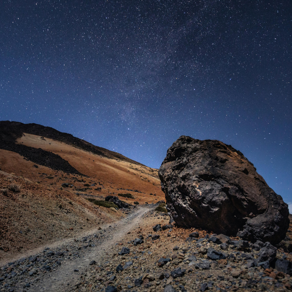 A large rock rests on a hillside against a backdrop of a star-filled night sky.