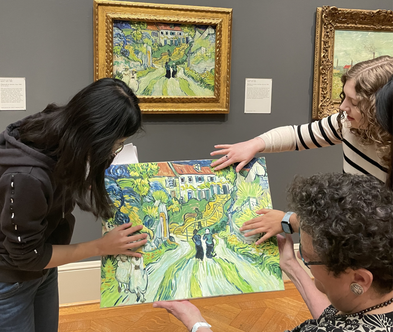 Three women touch facsimile of the Van Gogh painting Stairway at Auvers with the real painting in the background.