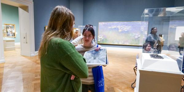 One woman offers another a handheld visual aid in the gallery of an art museum