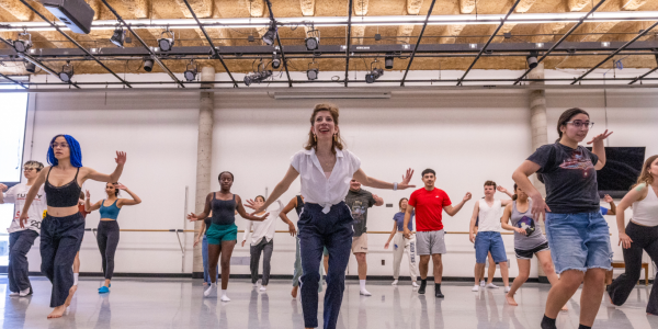 A diverse group of students in a WashU dance class, dressed in comfortable workout attire, practicing choreography together.