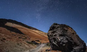 A large rock rests on a hillside against a backdrop of a star-filled night sky.